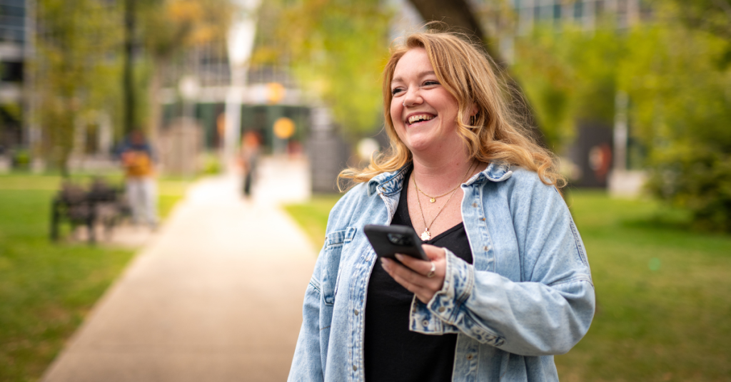 Woman in downtown Regina smiles while holding phone.